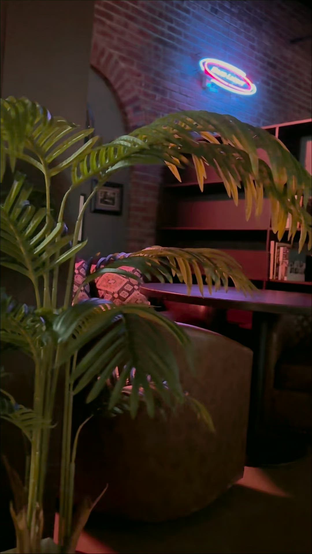 Dimly lit speakeasy lounge nook with leather chair, plant, bookshelf, and neon at KAOS Milford
