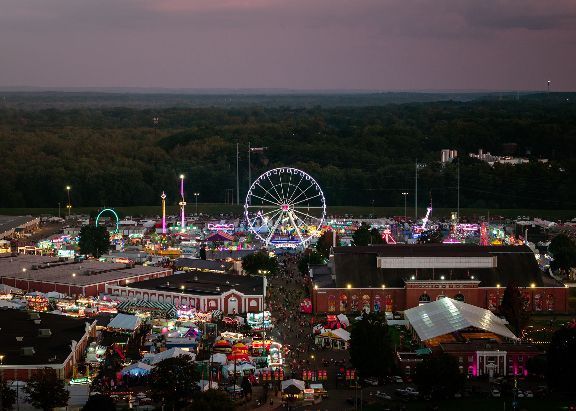 Aerial view of The Big E fairgrounds in West Springfield at dusk, with the Ferris wheel and midway lights